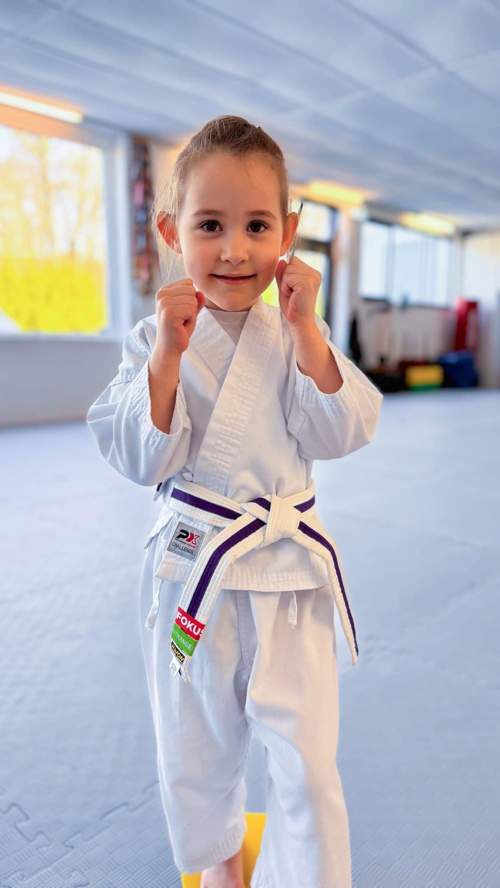 Lächelndes Kind im weißen Gi in Kampfhaltung im Dojo.